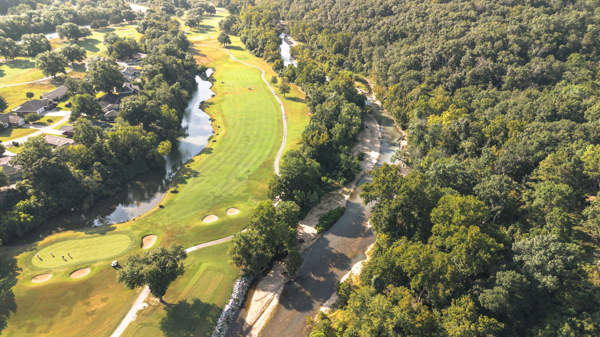 Aerial view of golf greens and fairways meeting forested shoreline